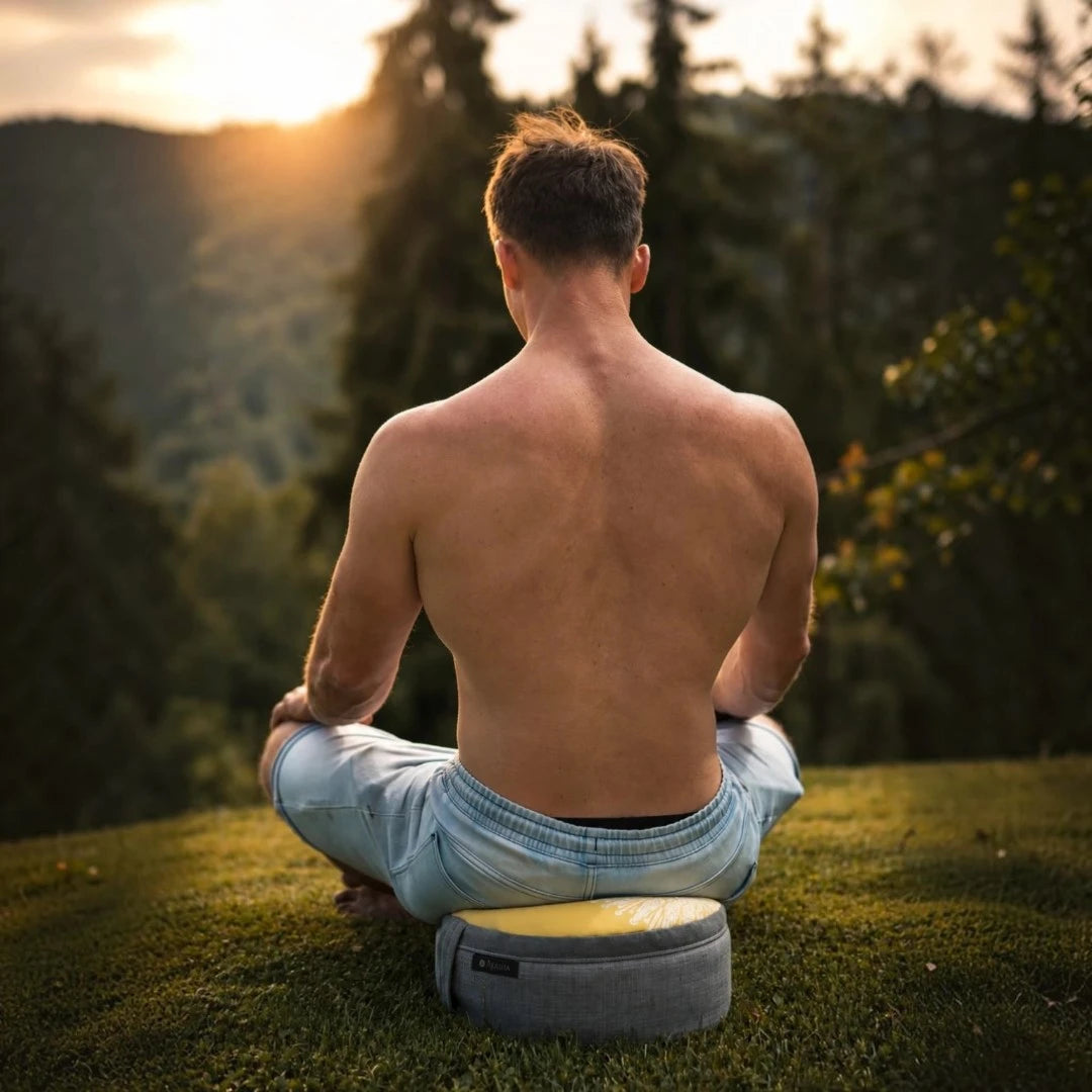 Man sitting on a meditation pillow outdoors with a sunset background