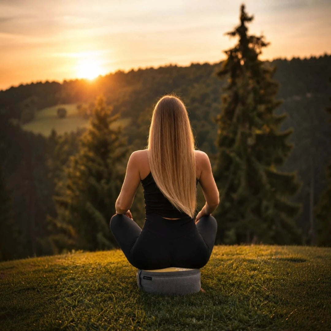 Woman meditating on a grassy hill with a scenic sunset view