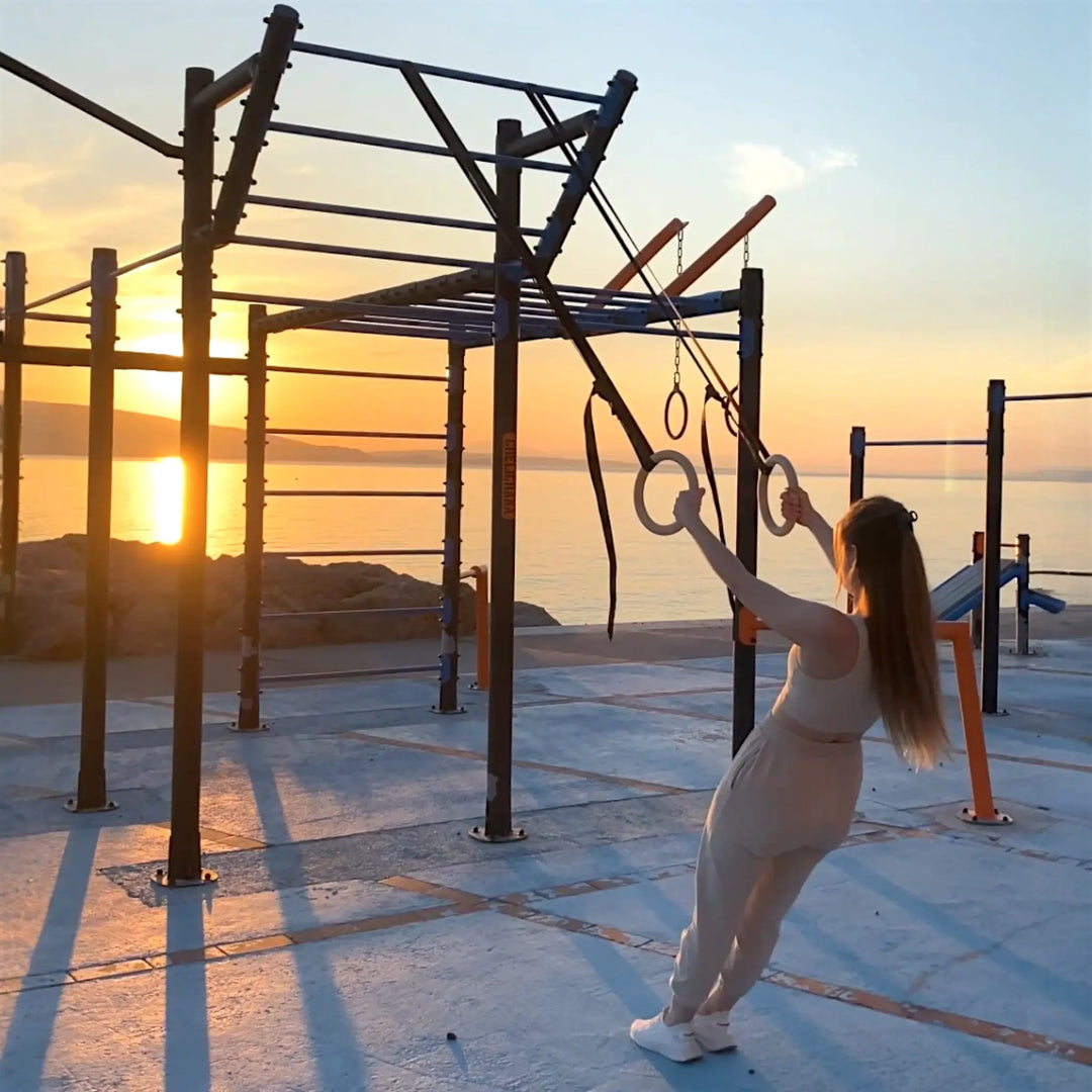 Girl exercising on outdoor fitness with gymnastic rings at sunset.