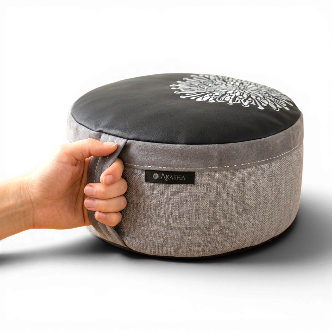 A person carrying a grey buckwheat meditation cushion by its durable fabric handle.
